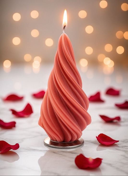 Pink twisted candle with a lit wick on a marble surface with red rose petals and blurred lights in the background.
